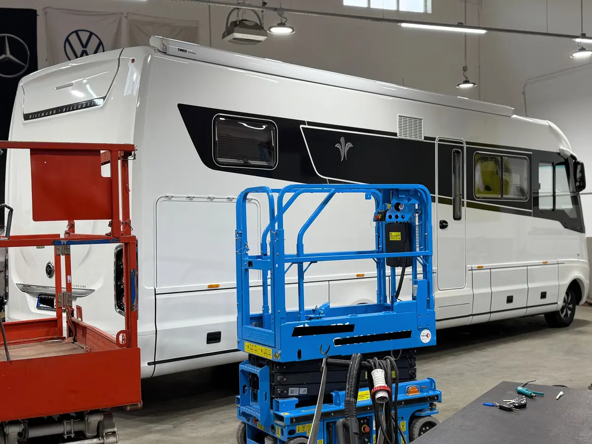 Wohnmobil in der Halle mit Scherenarbeitsbühne davor, um Dach und obere Flächen bei der Politur zu erreichen – KFZ-Aufbereitung Siebers